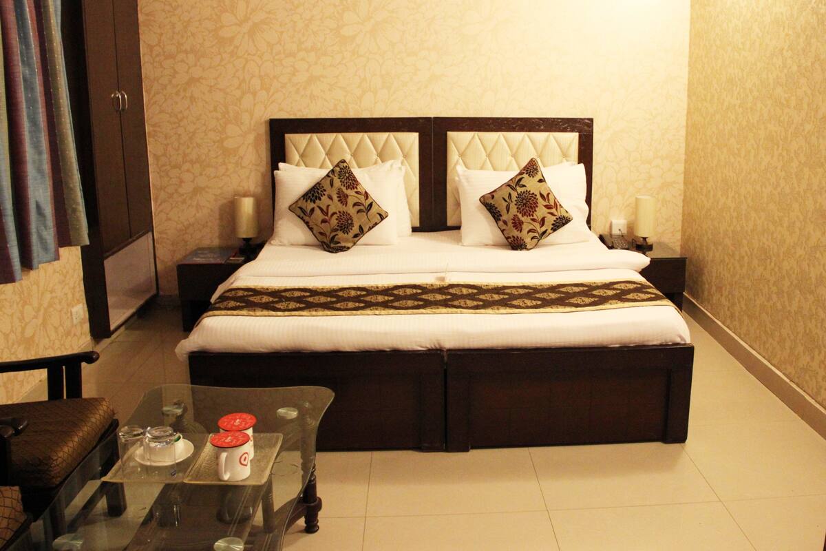 A hotel room with a bed, nightstands, a glass coffee table with a mug and glasses, and a chair.