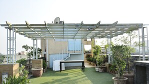 A rooftop terrace with artificial grass, a pergola, potted plants, and a staircase leading to an upper level.
