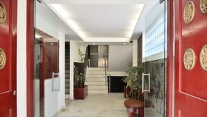 A modern hotel lobby with a marble floor, red doors, and a staircase leading to an upper level.