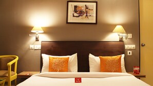 A hotel room with a large bed, two pillows with tree designs, a framed artwork on the wall, and two bedside lamps.