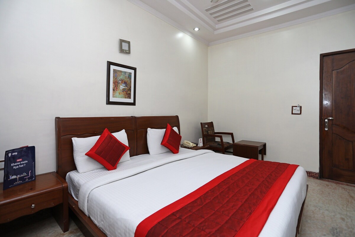 A neatly made bed with a red and white bedspread, a wooden headboard, and a small bedside table with a lamp.