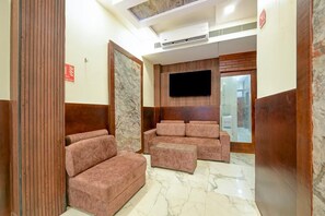 A modern living room with a flat-screen TV mounted on the wall, a seating area with sofas and ottomans, and a marble floor.