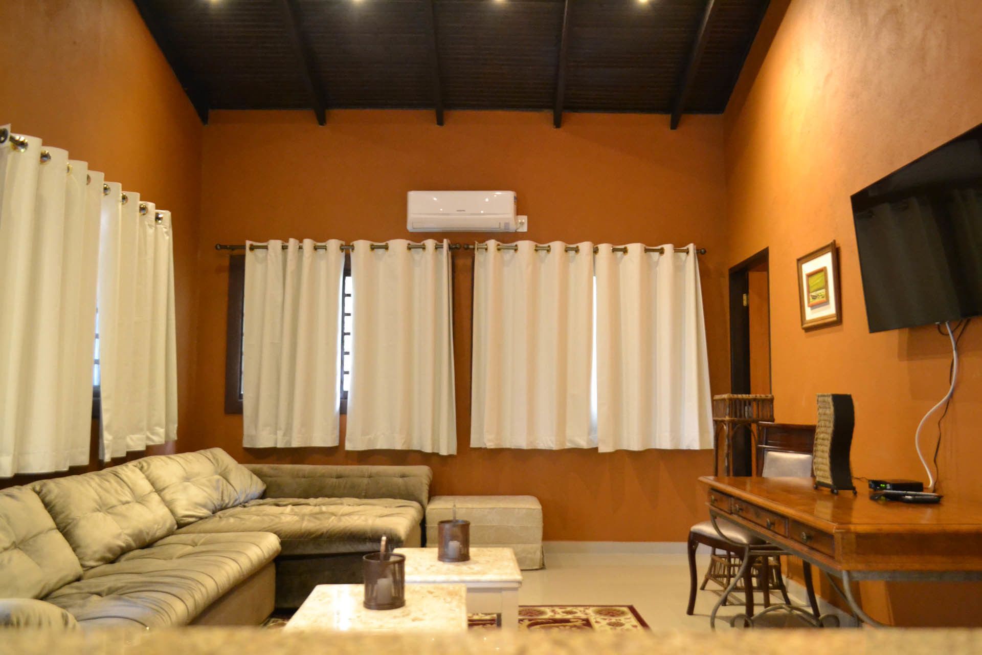 Una sala de estar con sofá, una mesa de centro, televisor y cortinas.