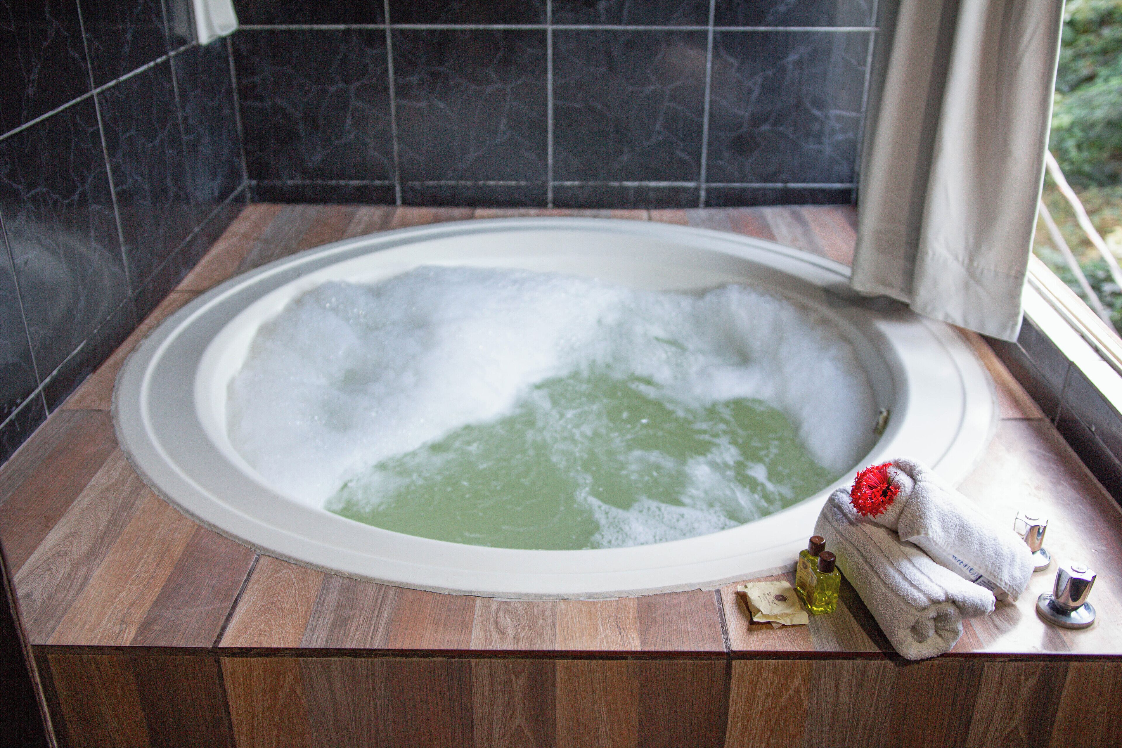 A bathtub with a wooden floor, a towel, and a bottle of lotion.