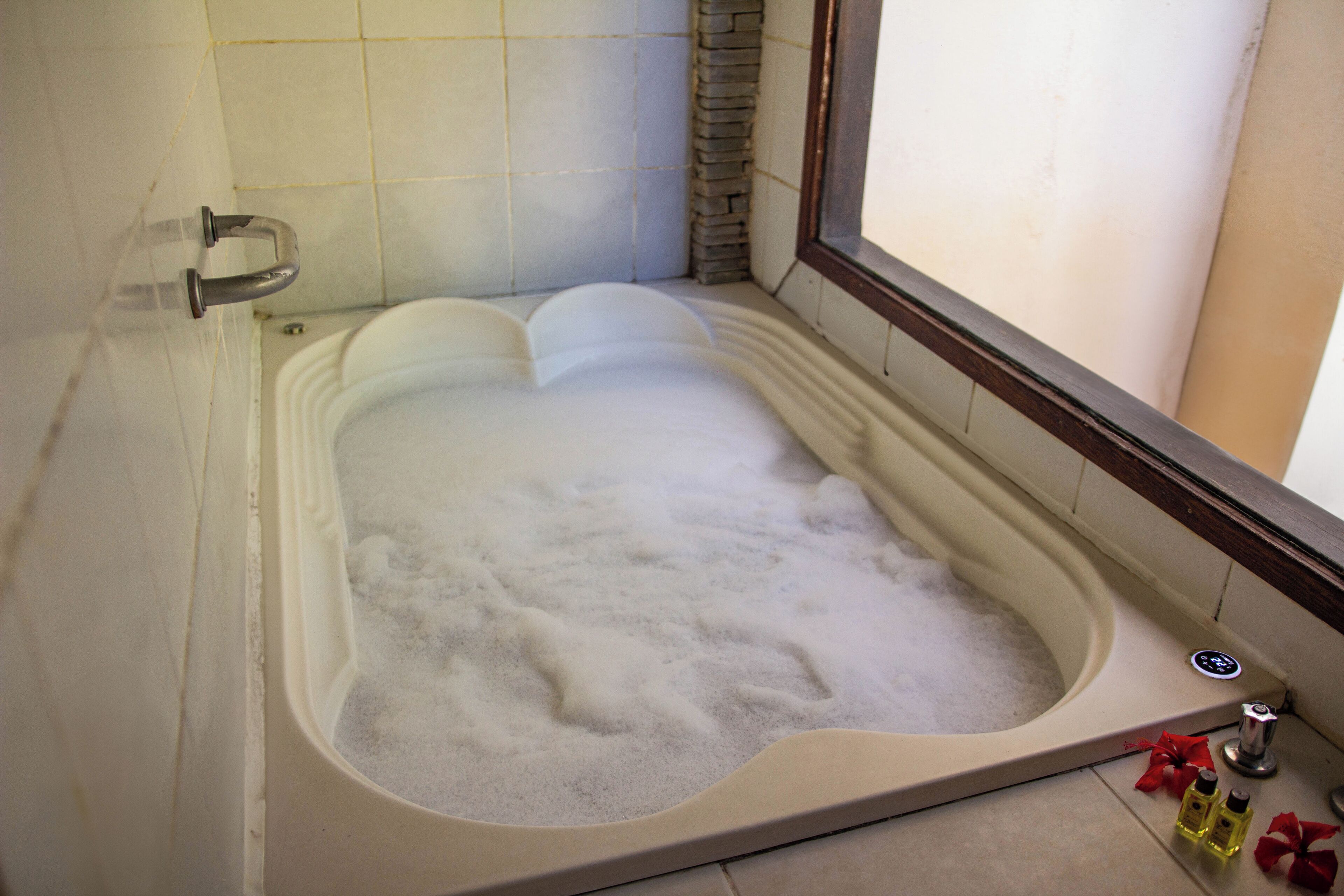 A large bathtub filled with bubbles, a window, and a showerhead.