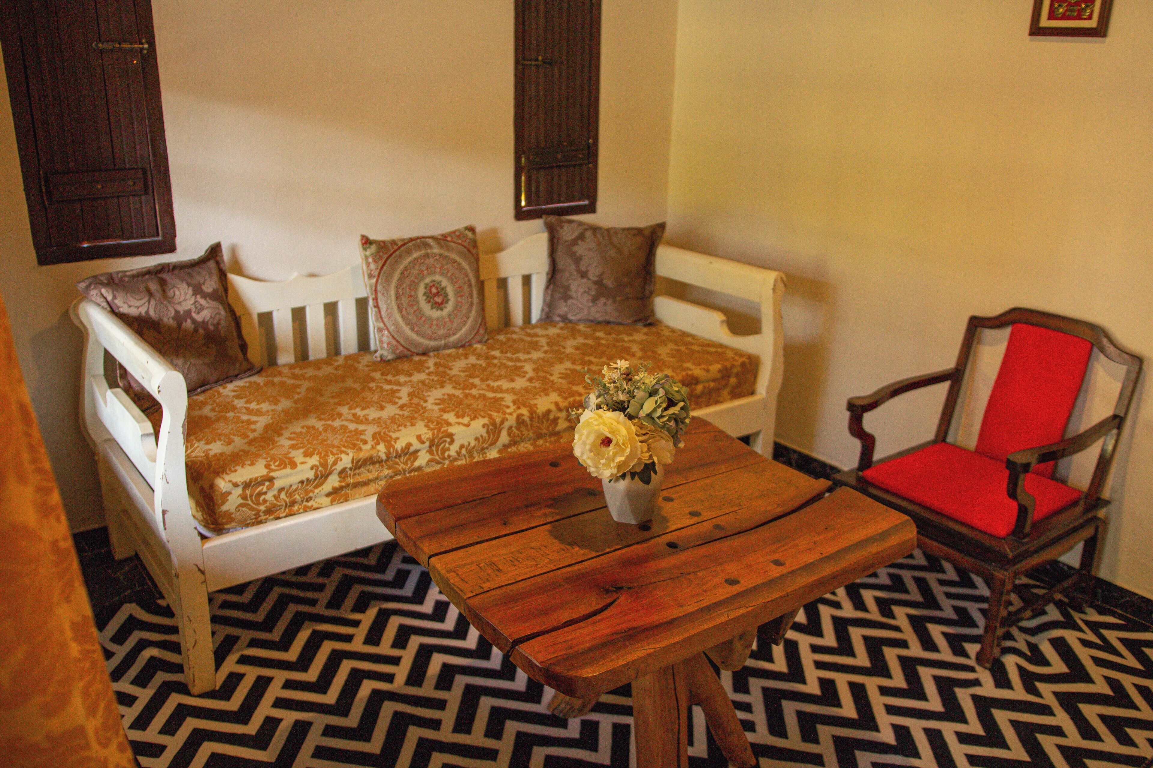 A room with a sofa, a wooden table with a vase of flowers, a red chair, and patterned flooring.