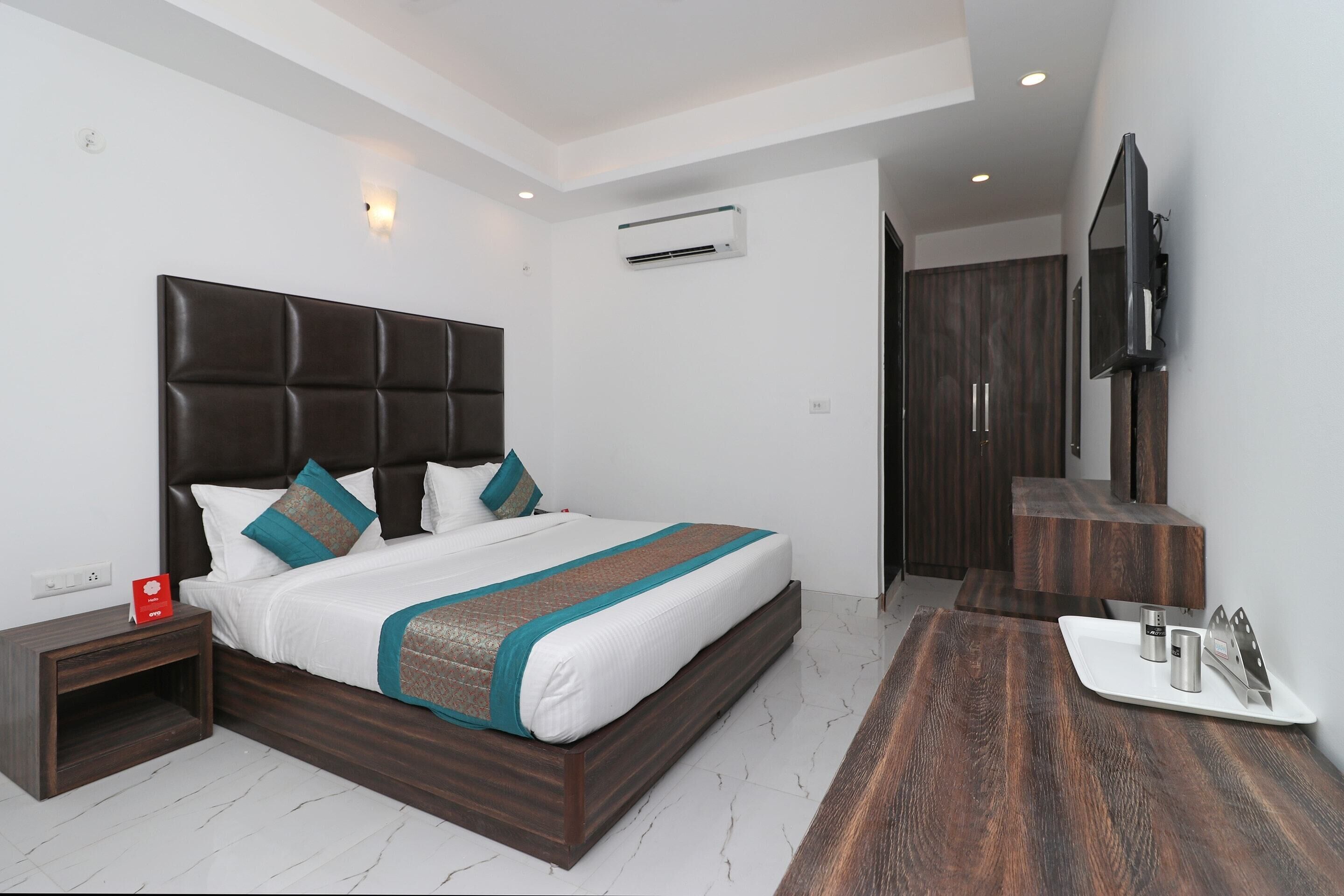A modern hotel room with a large bed, a wooden nightstand, a bedside table, a flat-screen TV, and a small table with a tray.