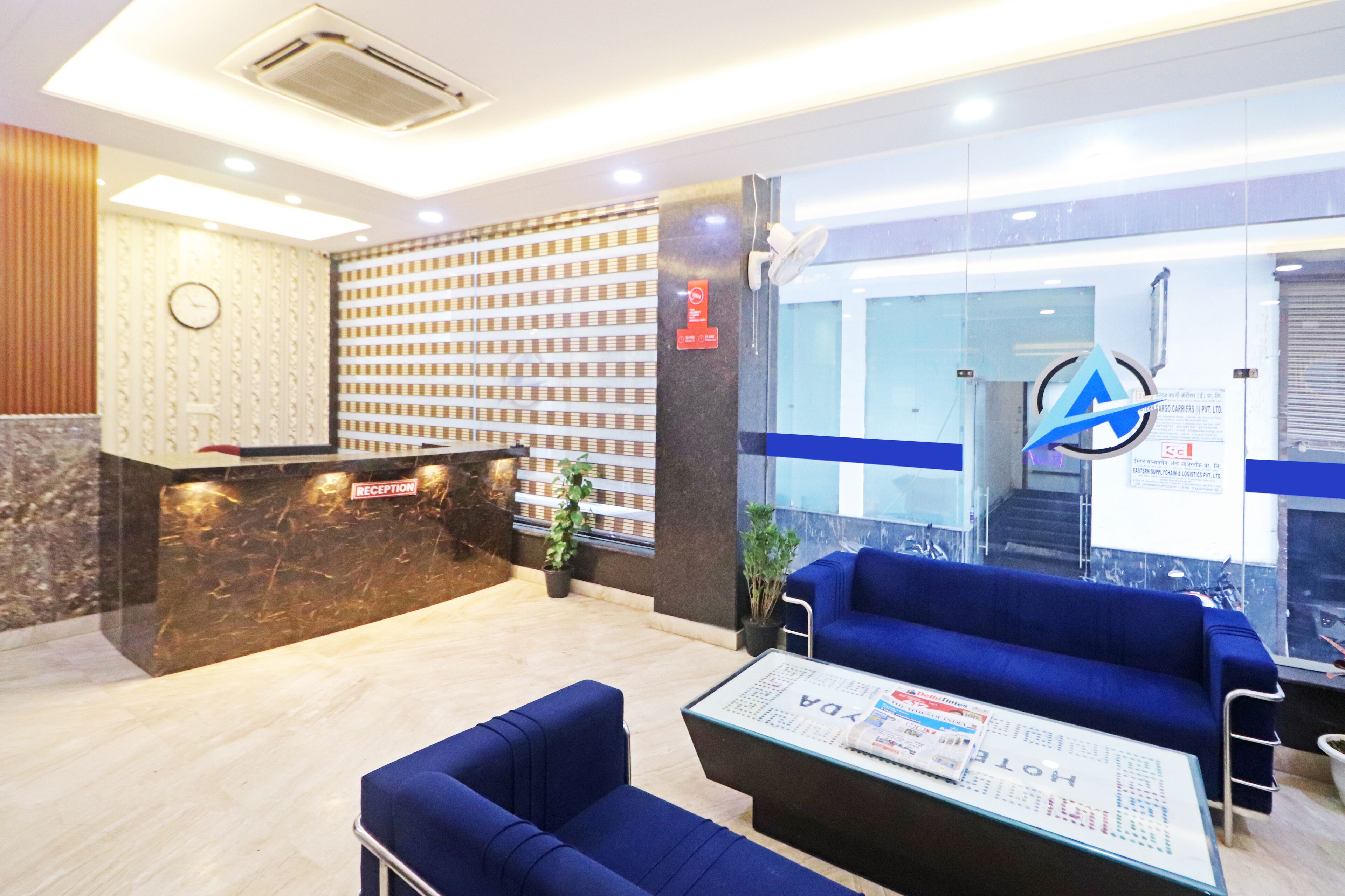 A reception area with a marble counter, blue seating, and a glass wall with a logo.