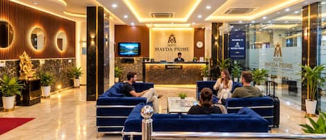 Zona de recepción de un hotel con mostrador, asientos y televisor.