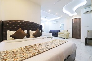 A modern hotel room with a large bed, a sofa, a chair, and a desk. - Hotel Mayda Prime Near Delhi Airport (New Delhi)