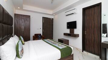 A modern bedroom with a large bed, dark wooden wardrobe, a mounted TV, and an air conditioning unit.