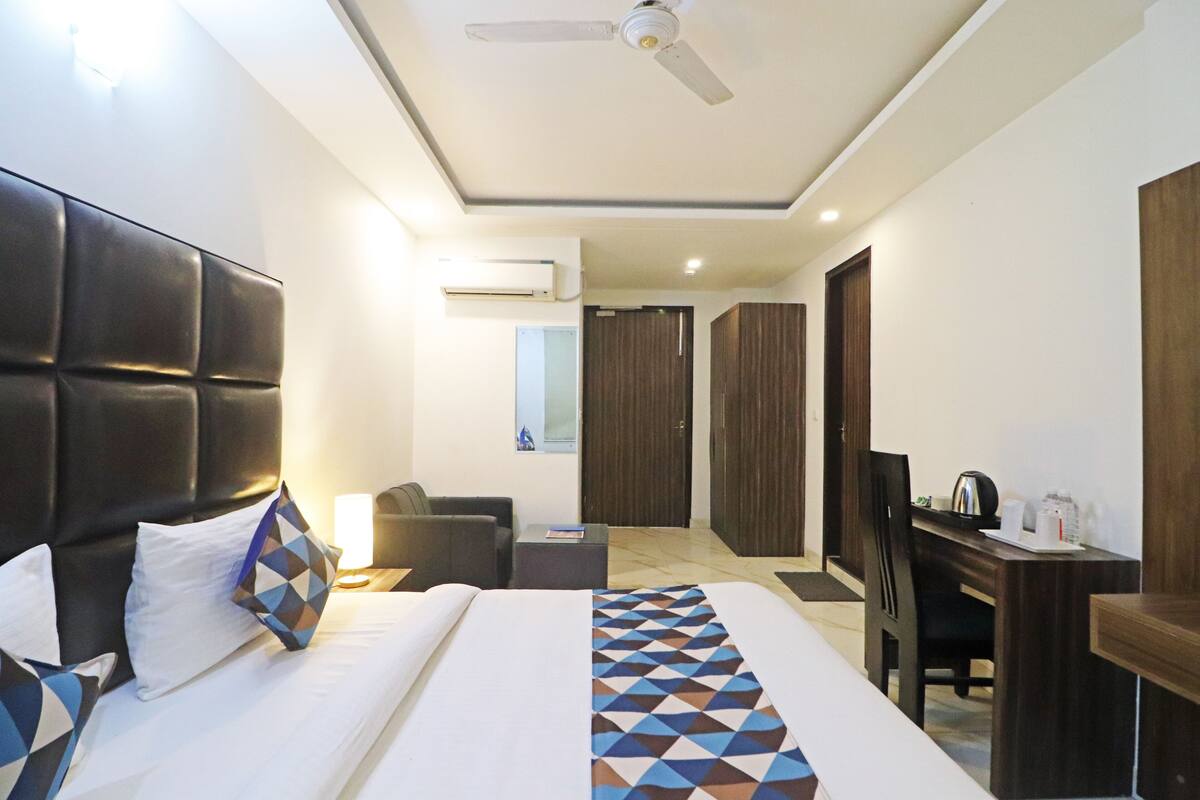 A hotel room with a large bed, a desk, a chair, a ceiling fan, and a wardrobe.