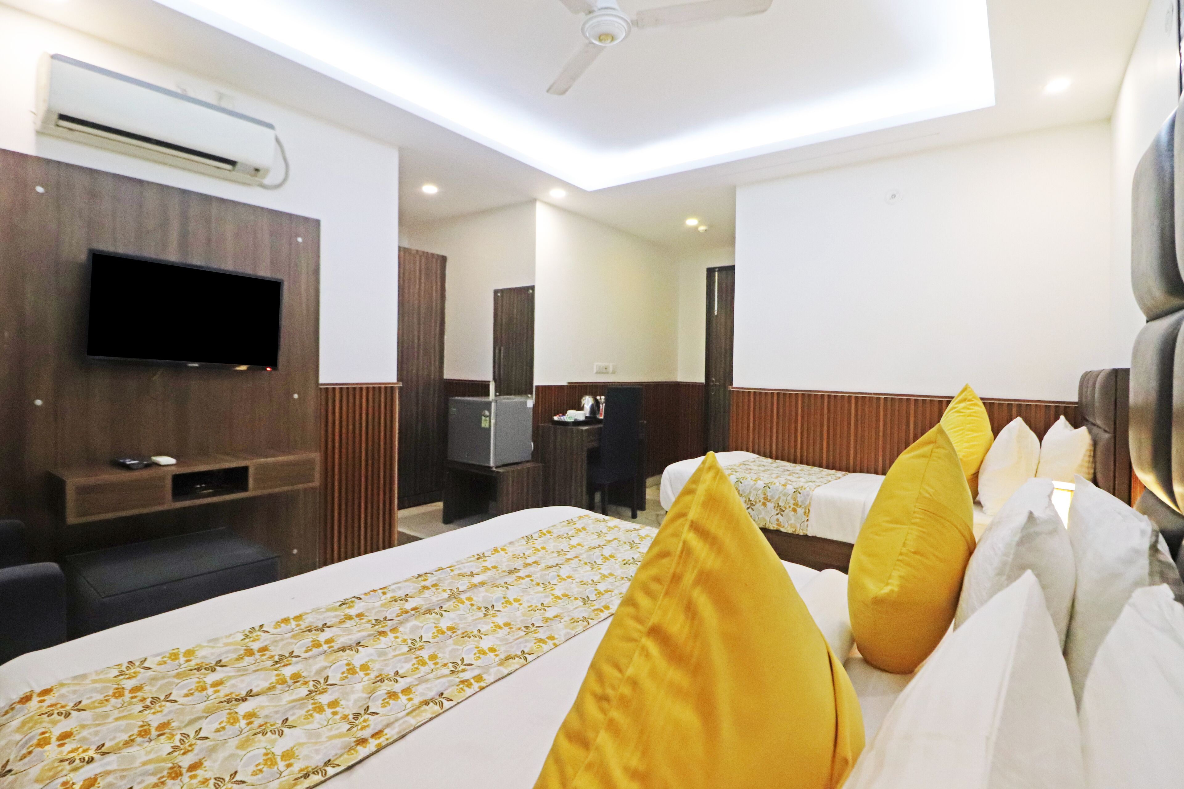 A hotel room with a large bed, a flat-screen TV mounted on the wall, a desk with a chair, and an air conditioning unit.