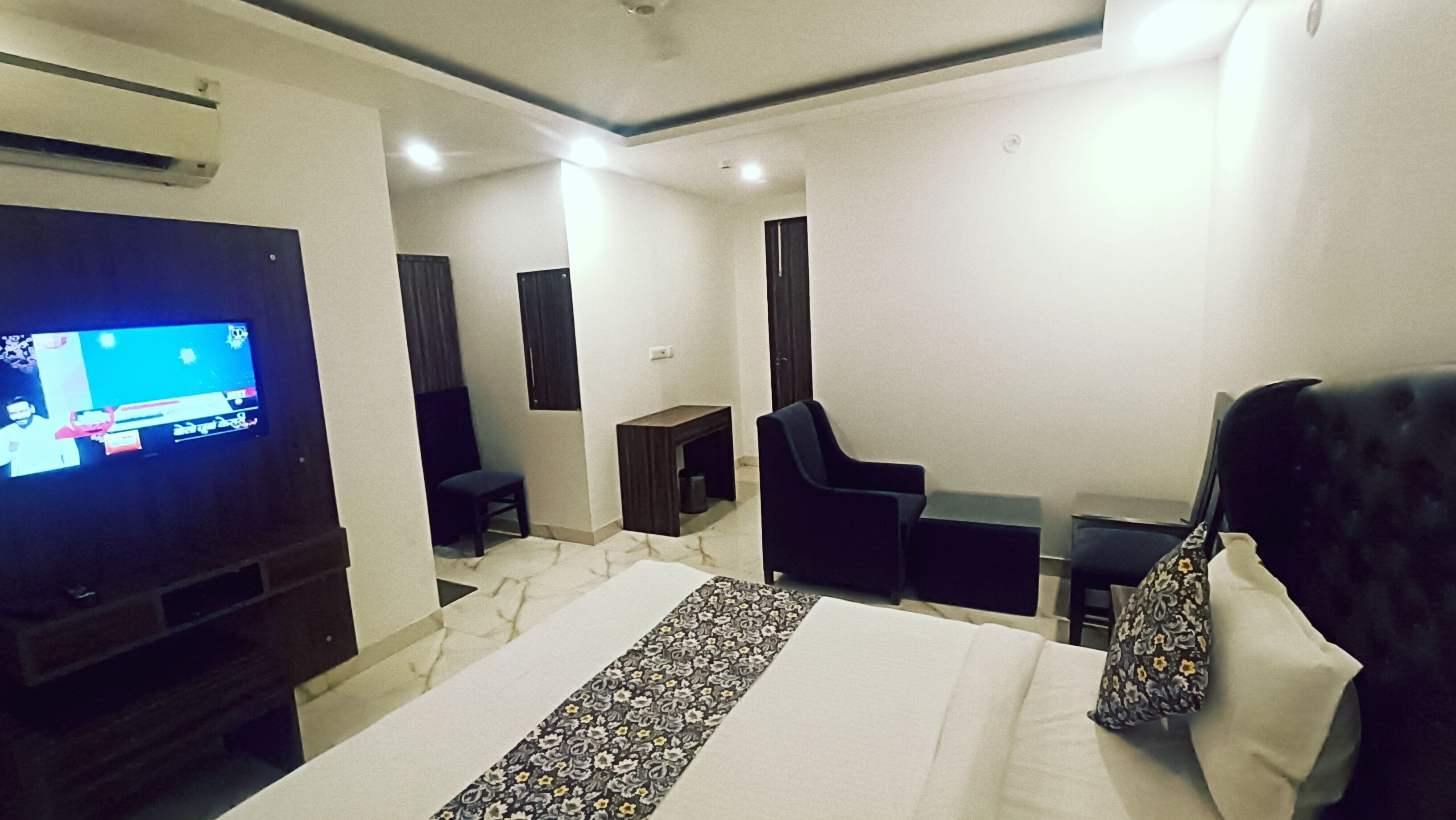 A hotel room with a bed, a TV, a desk, a chair, and a small table.