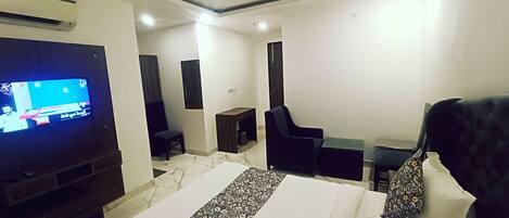 A hotel room with a bed, a TV, a desk, a chair, and a small table.