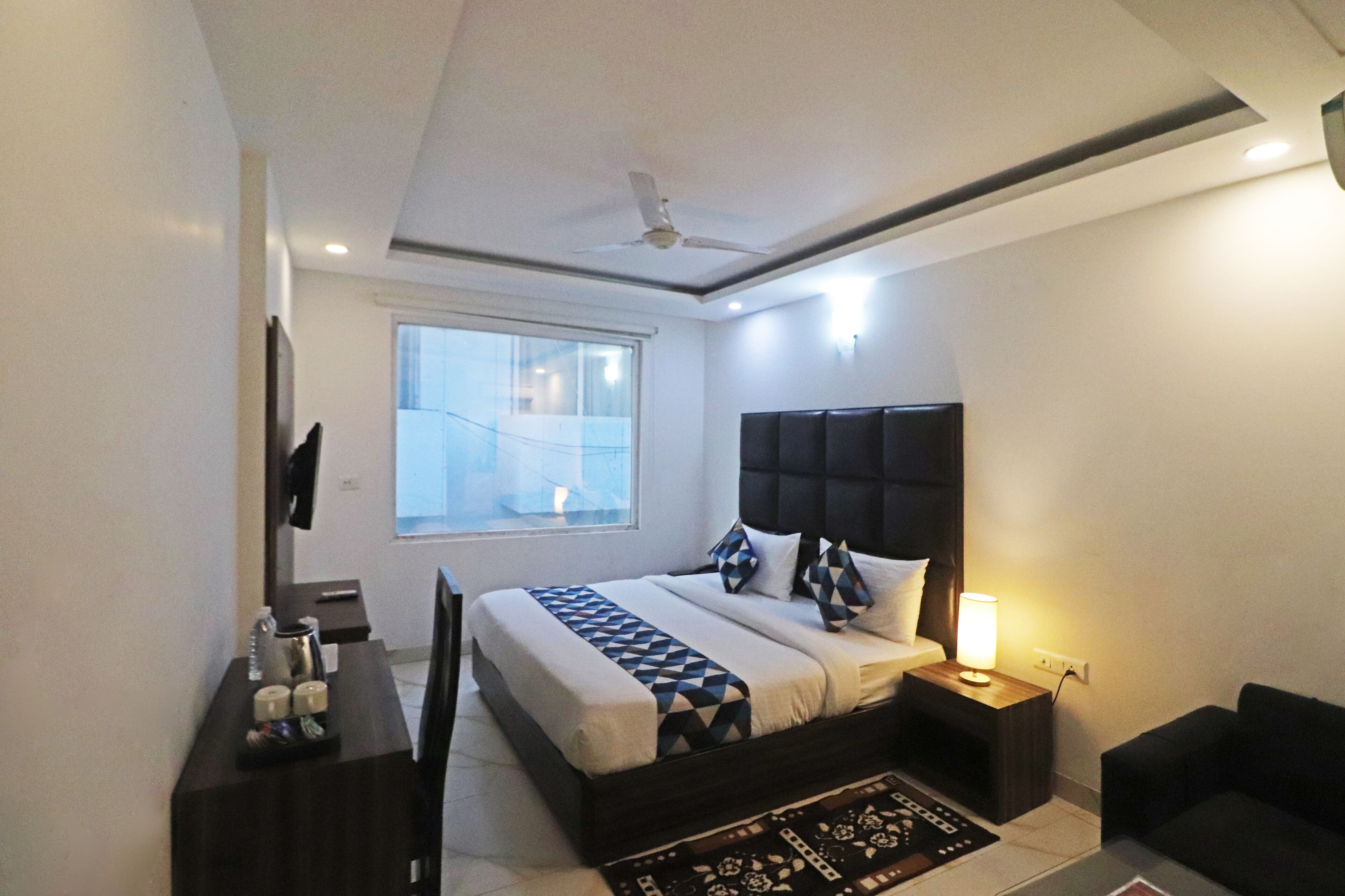 Een moderne slaapkamer met een bed, nachtkastje, lamp en uitzicht naar buiten door een raam.
