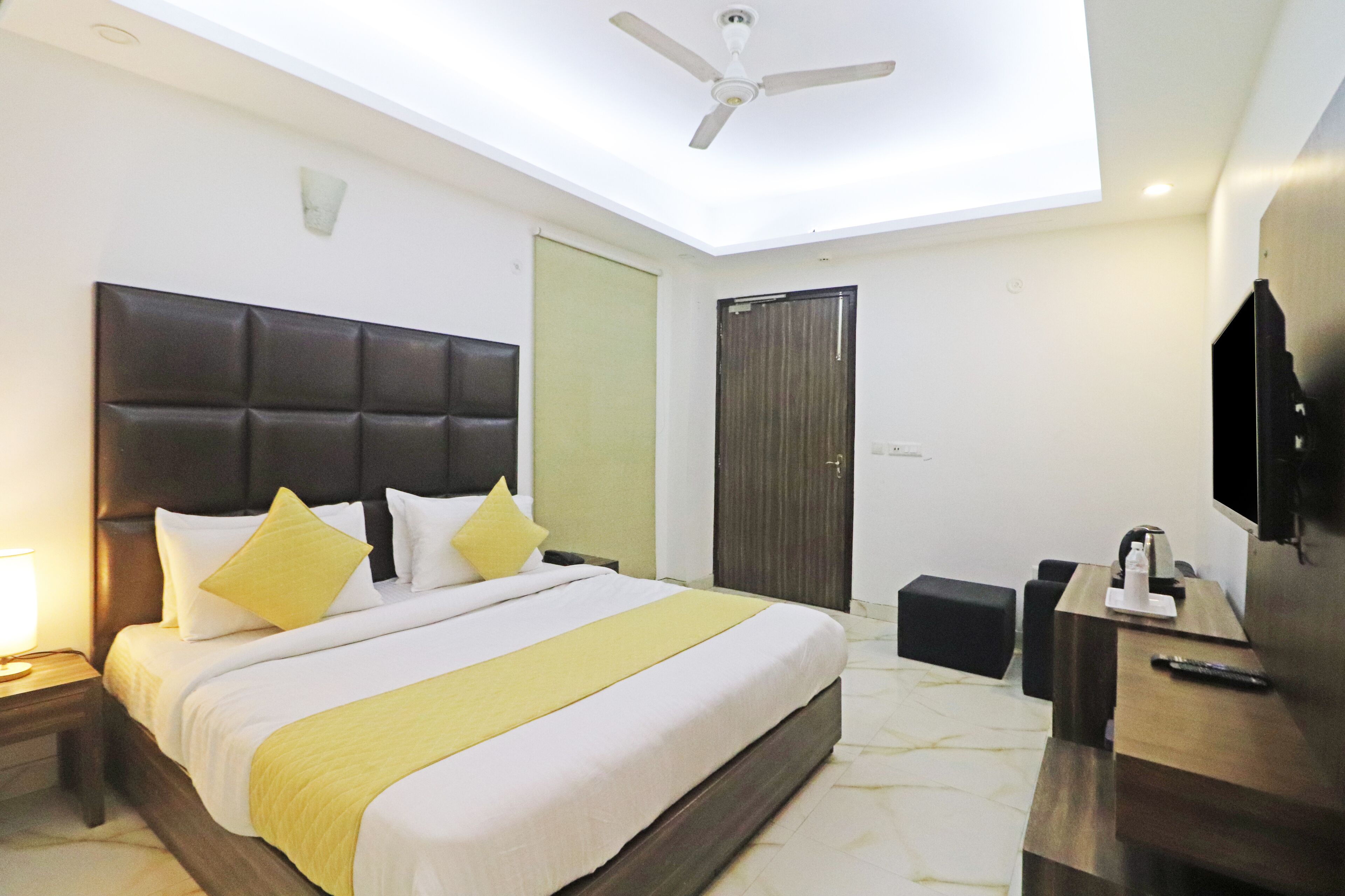 A hotel room with a large bed, a desk, a chair, a TV, a ceiling fan, and a door.