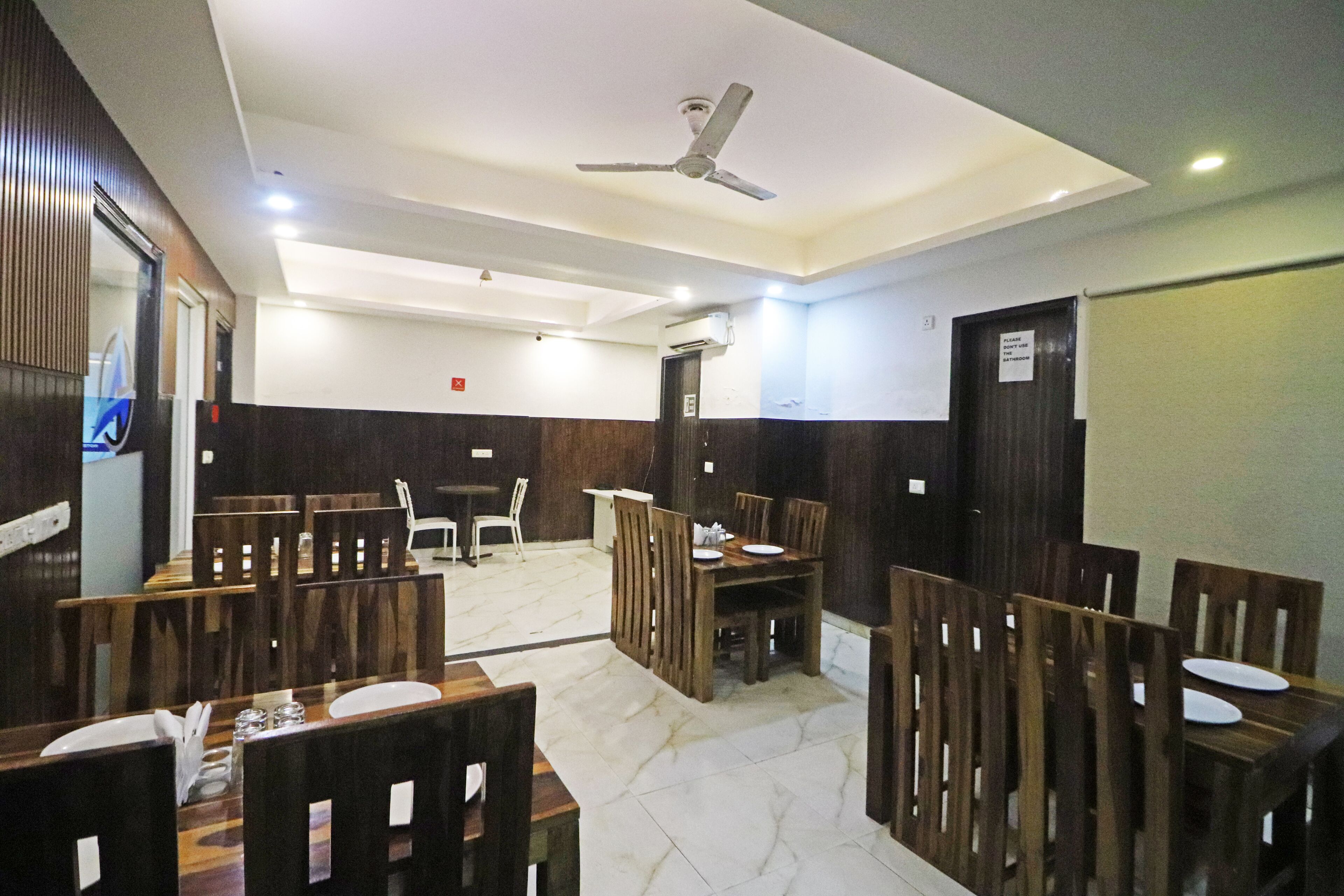 Un espace repas avec des tables et des chaises en bois, un ventilateur de plafond et un sol carrelé.