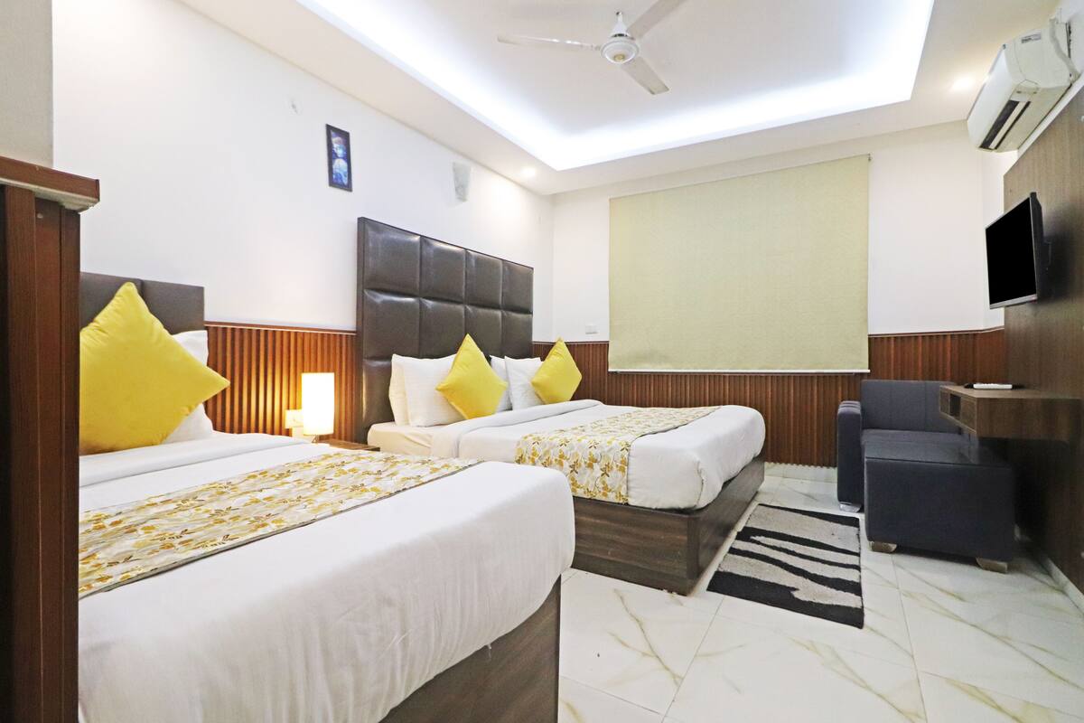 A hotel room with two beds, a desk, a chair, a TV, and a ceiling fan.
