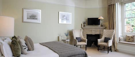 A bedroom with a bed, two armchairs, a fireplace, and a television.