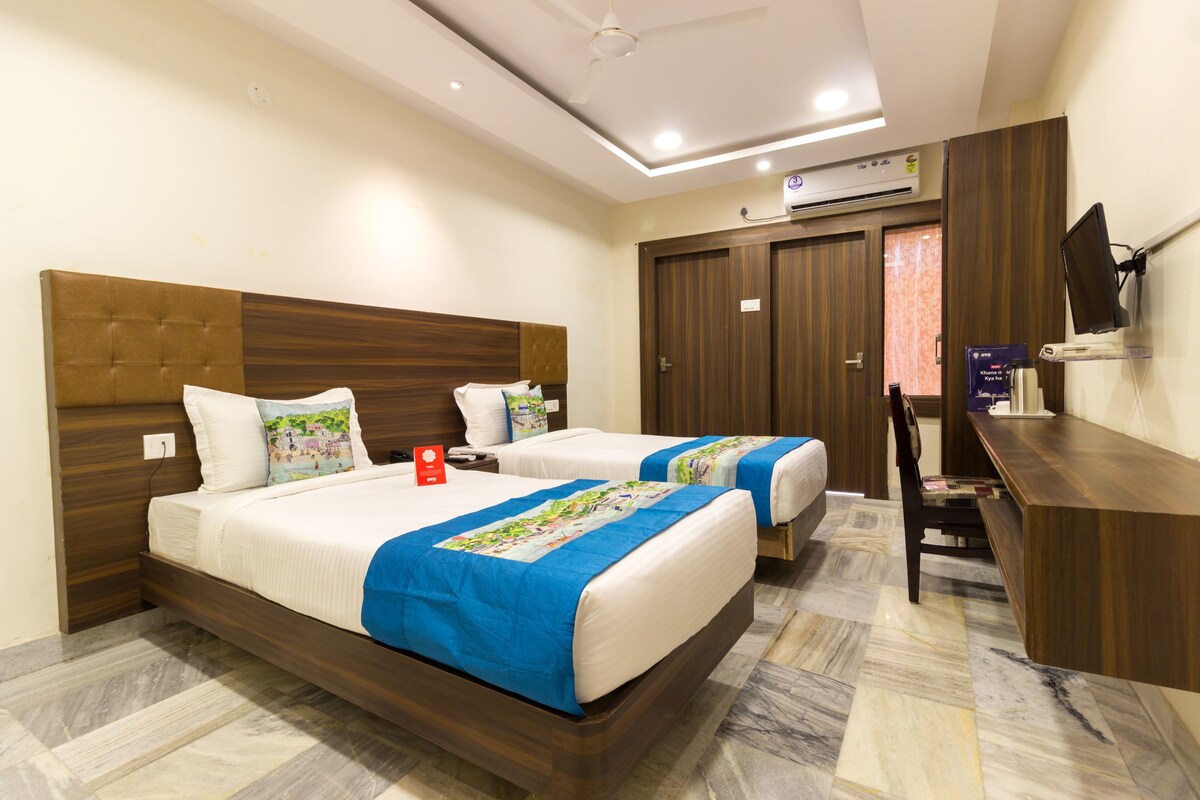 A hotel room with two beds, a desk, a chair, and a TV.
