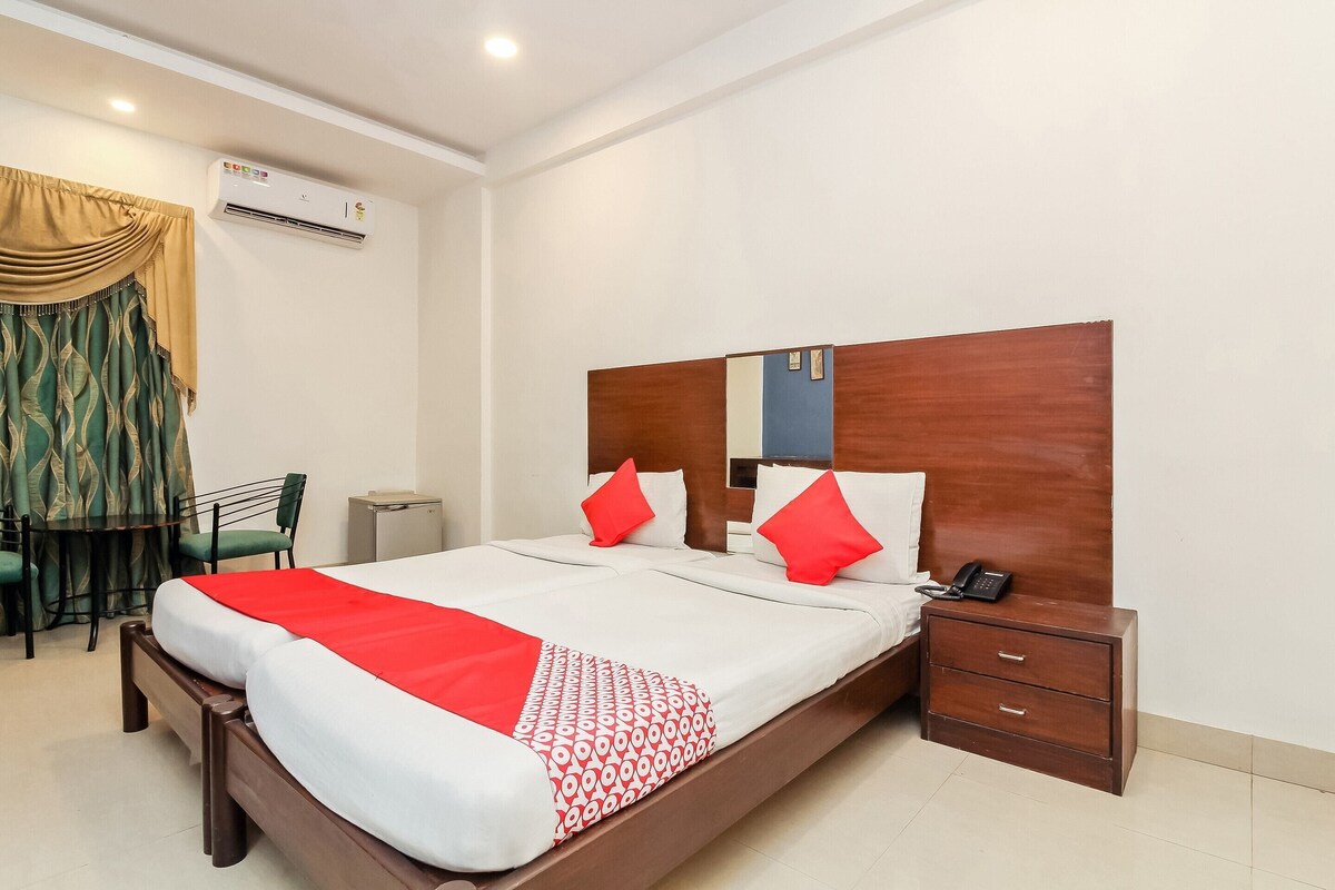 A hotel room with a large bed, a wooden headboard, a bedside table with a phone, and a desk with a chair.