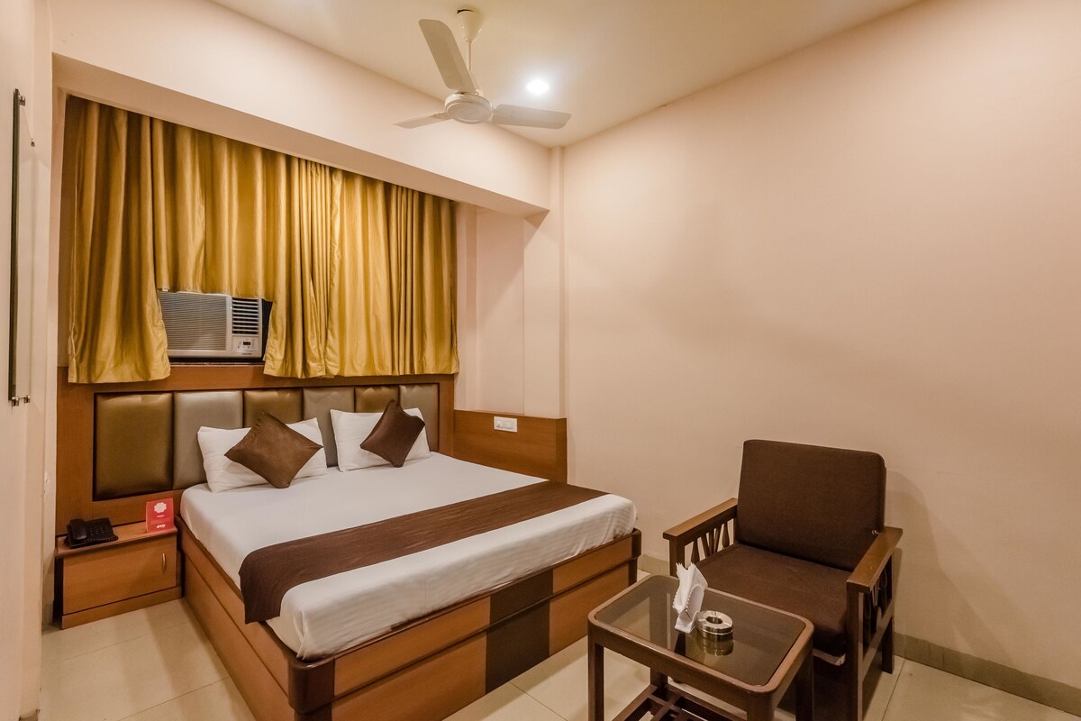 A hotel room with a bed, bedside table, chair, and a ceiling fan.