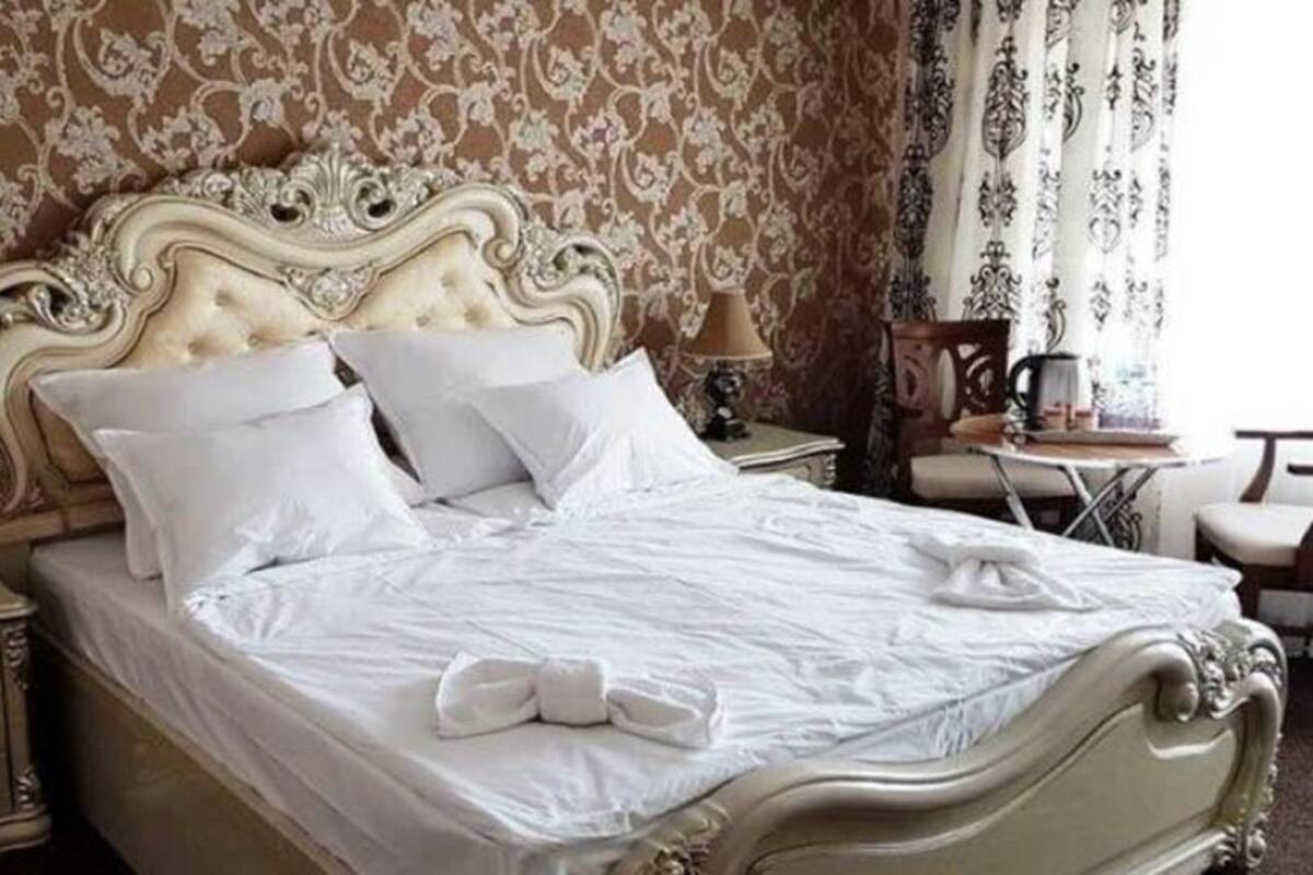 A classic four-poster bed with white linens and pillows, a nightstand with a lamp, and a small table with a cup and saucer.