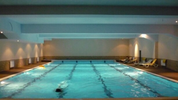 An indoor swimming pool with lane dividers, lounge chairs, and a swimmer in the water. - Elit Palace Hotel & Spa (Balchik)