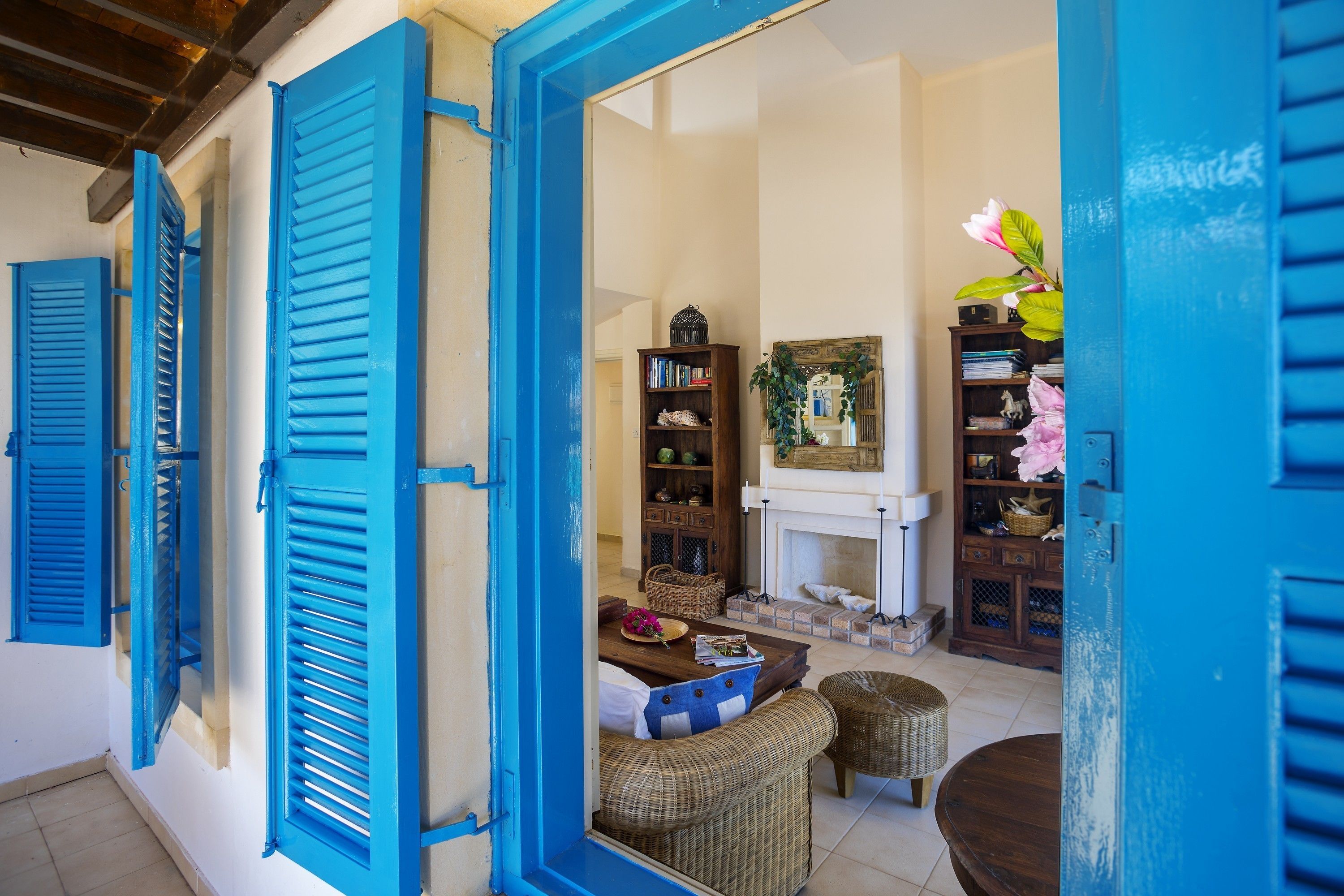 A room with blue shutters, wicker furniture, a fireplace, and a bookshelf.