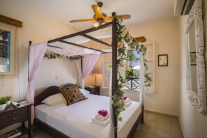 A four-poster bed with a ceiling fan, a bedside table with a lamp, and a window with curtains. - Protaras Villa Ayios Elias Views (Paralimni)