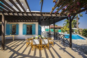 Un área de comedor al aire libre cubierta con una piscina al fondo.