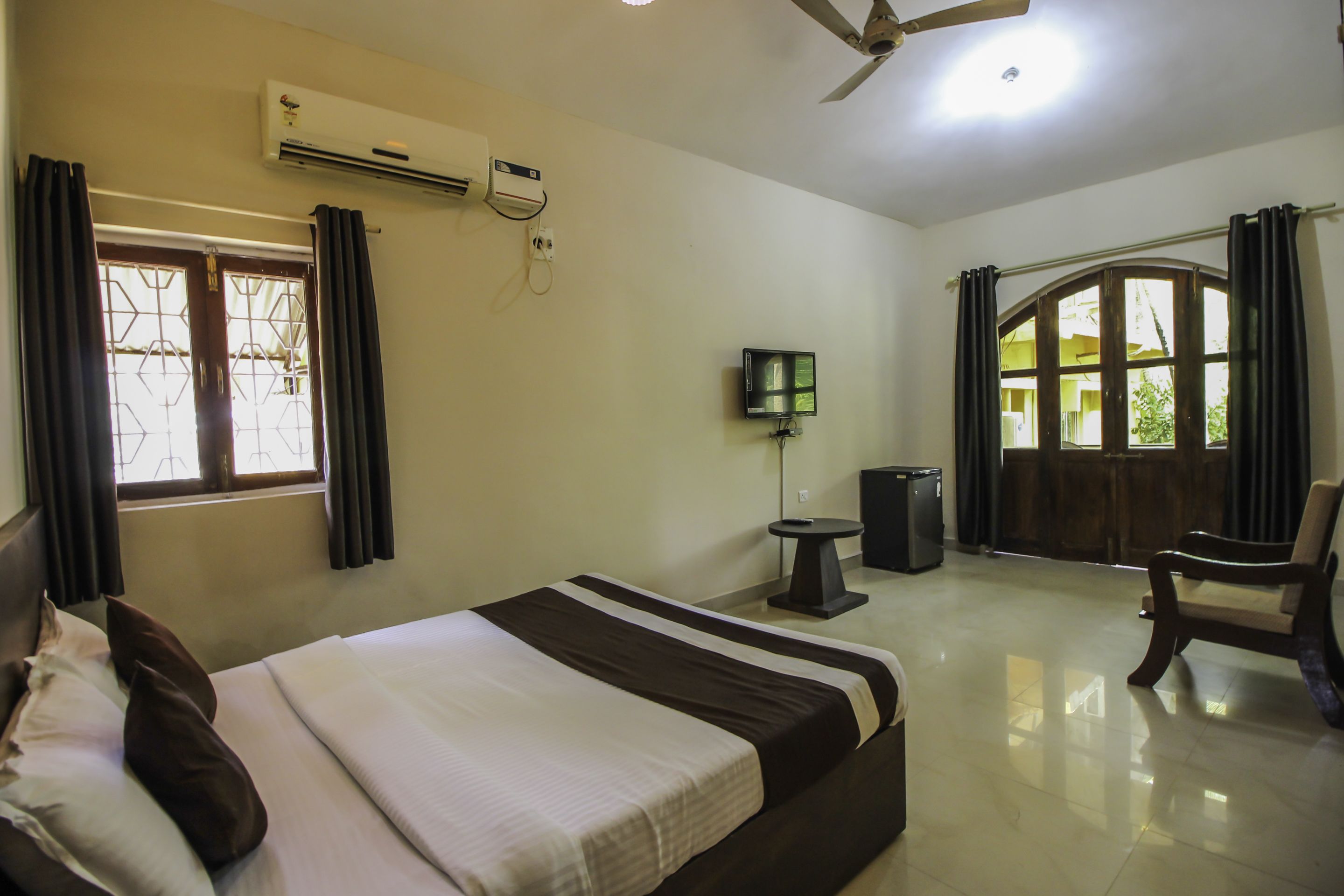 A hotel room with a bed, a desk, a chair, an air conditioner, a TV, and a window with curtains.