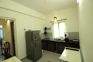 A compact kitchen with a refrigerator, sink, and a small dining table. - OYO 9365 Home Duplex 3 BHK Calangute North Goa (Calangute)