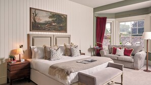 A bedroom with a large bed, a bedside table, a reading chair, a window with curtains, and a painting on the wall. - King John Inn (Salisbury)
