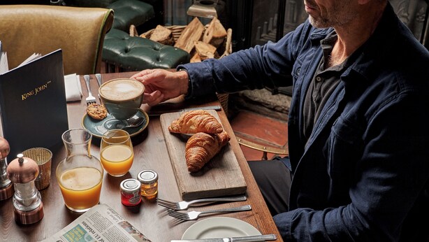 A breakfast setting with a croissant, coffee, and newspaper on a wooden table. - King John Inn (Salisbury)