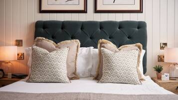 A neatly made bed with patterned pillows, a dark green headboard, and framed botanical prints on the wall.