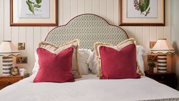 A neatly made bed with two red pillows, a headboard with a patterned design, and two framed botanical illustrations on the wall.