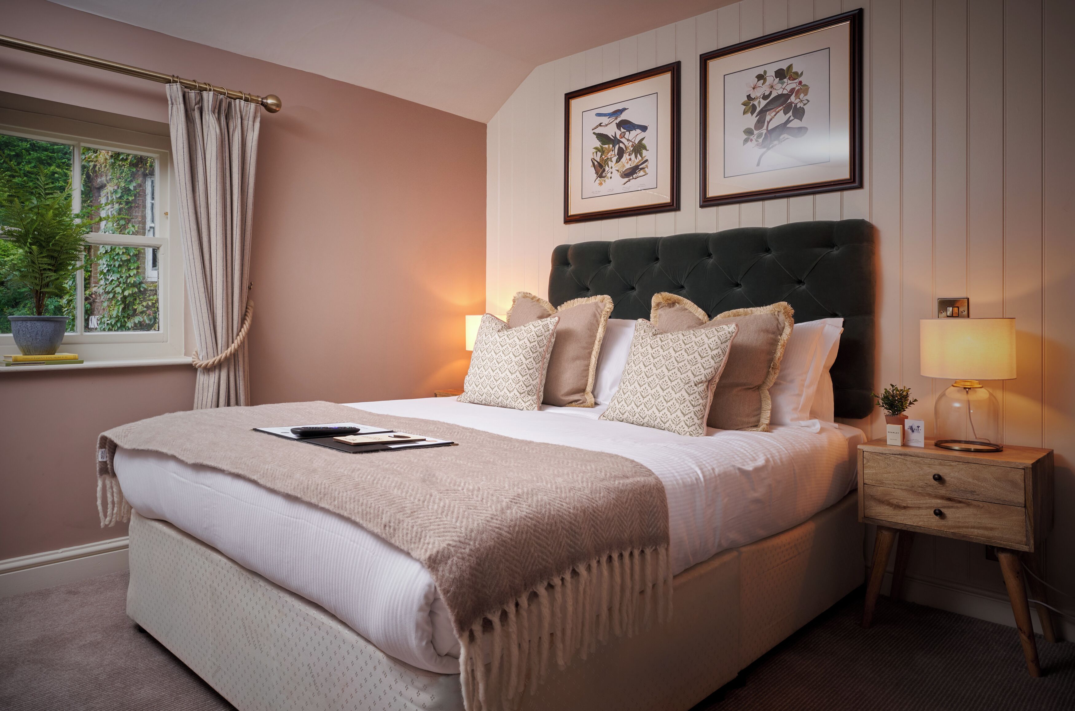 A neatly made bed with a headboard, bedside tables, and a window with curtains.