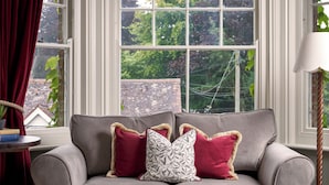 A grey sofa with patterned and solid red cushions, a small round table with books, and a lamp. - King John Inn (Salisbury)