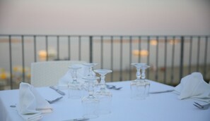 Mesa preparada para una comida, con copas de vino y cubiertos, con vistas a una barandilla y una masa de agua.