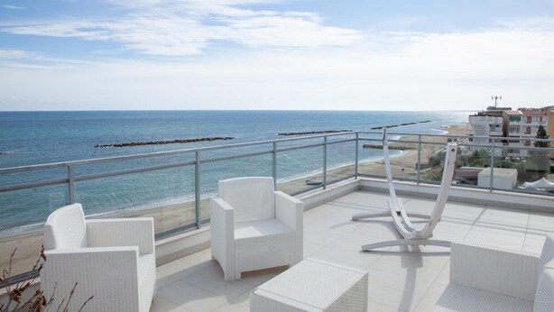 Terraço no telhado com mobiliário de vime branco, com vista para uma praia e o mar.