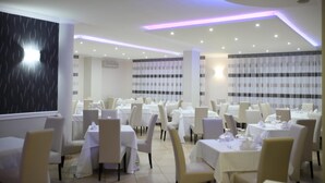 Restaurante com várias mesas e cadeiras, toalhas de mesa brancas e design de teto moderno com iluminação embutida.