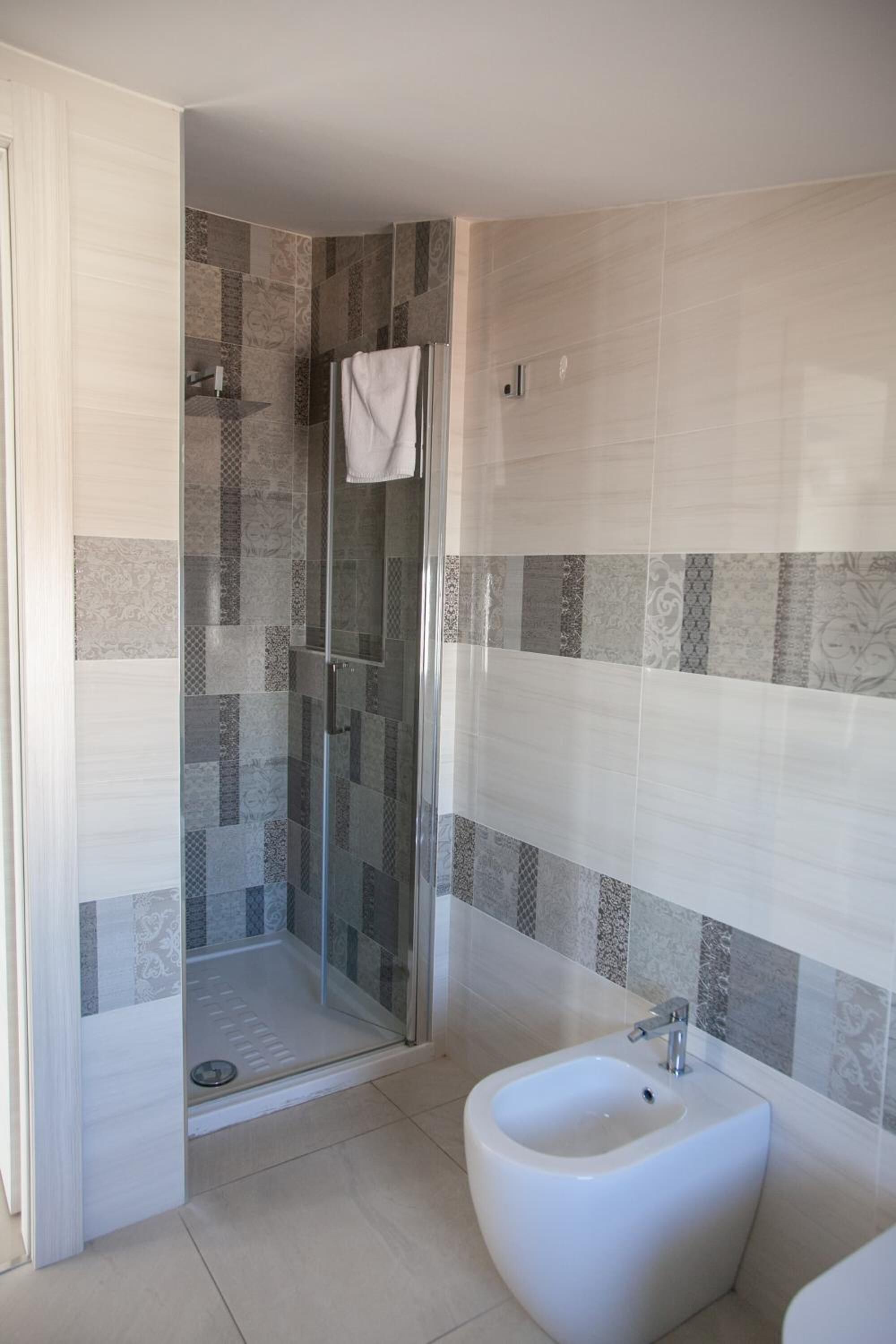 Ein modernes Badezimmer mit einer Glasdusche, einem Bidet und gemusterten Fliesen.