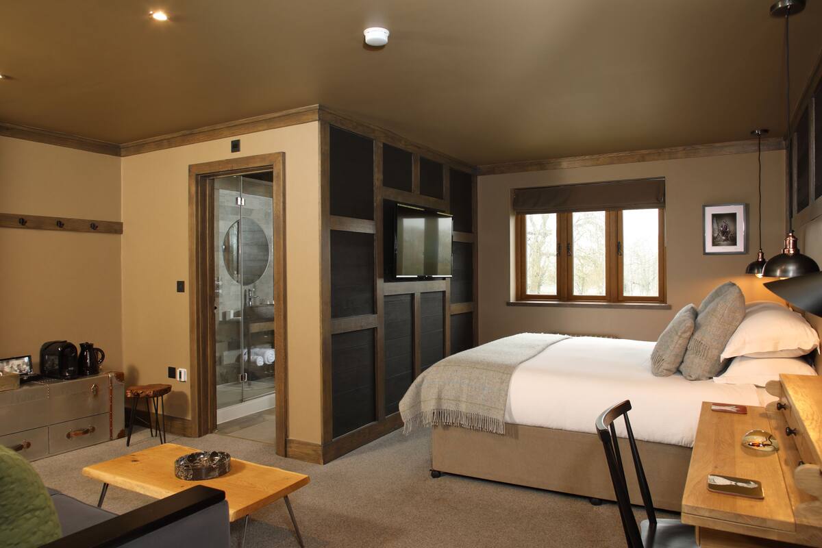 A bedroom with a bed, a desk, a chair, a small table, a coffee maker, and a window.