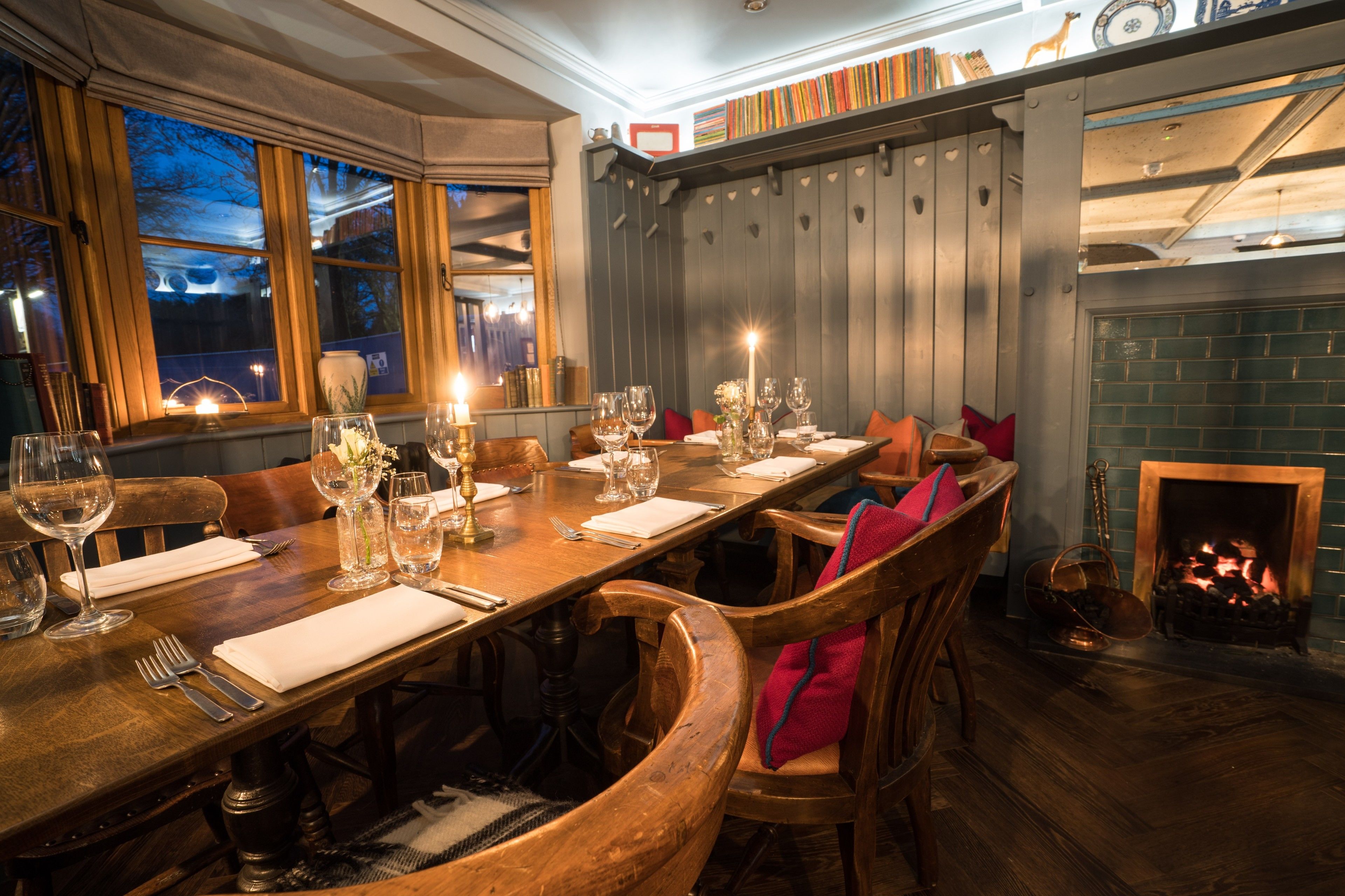 A dining area with a long wooden table set for a meal, surrounded by wooden chairs with red cushions.