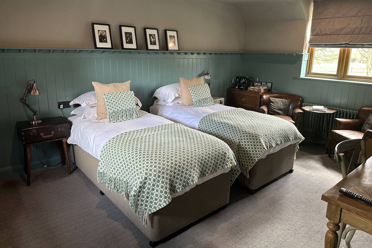 A room with two beds, a small table, a chair, and a window.