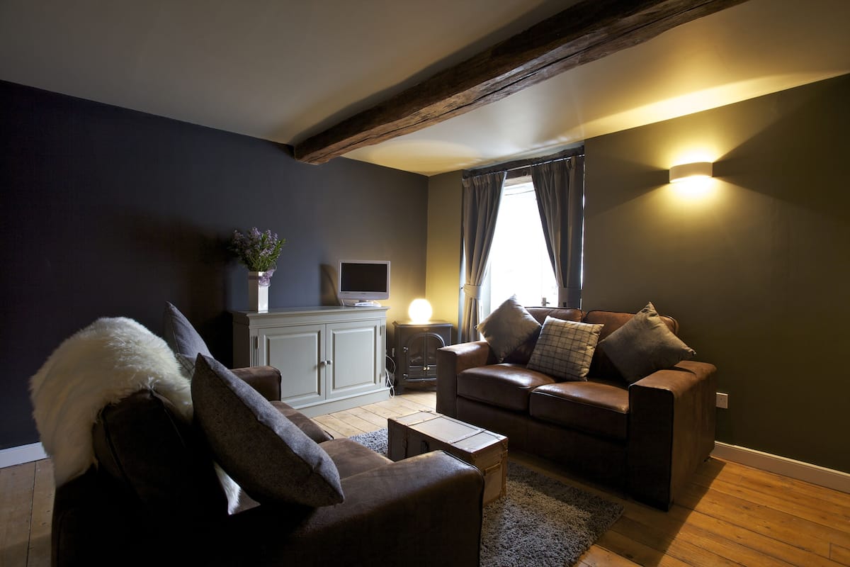 A living room with a brown leather sofa, a white cabinet, a television, and a wooden floor.