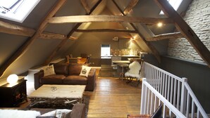 An attic living space with a loft bed, a sofa, a coffee table, and a fireplace. - The Kings Arms (Badminton)