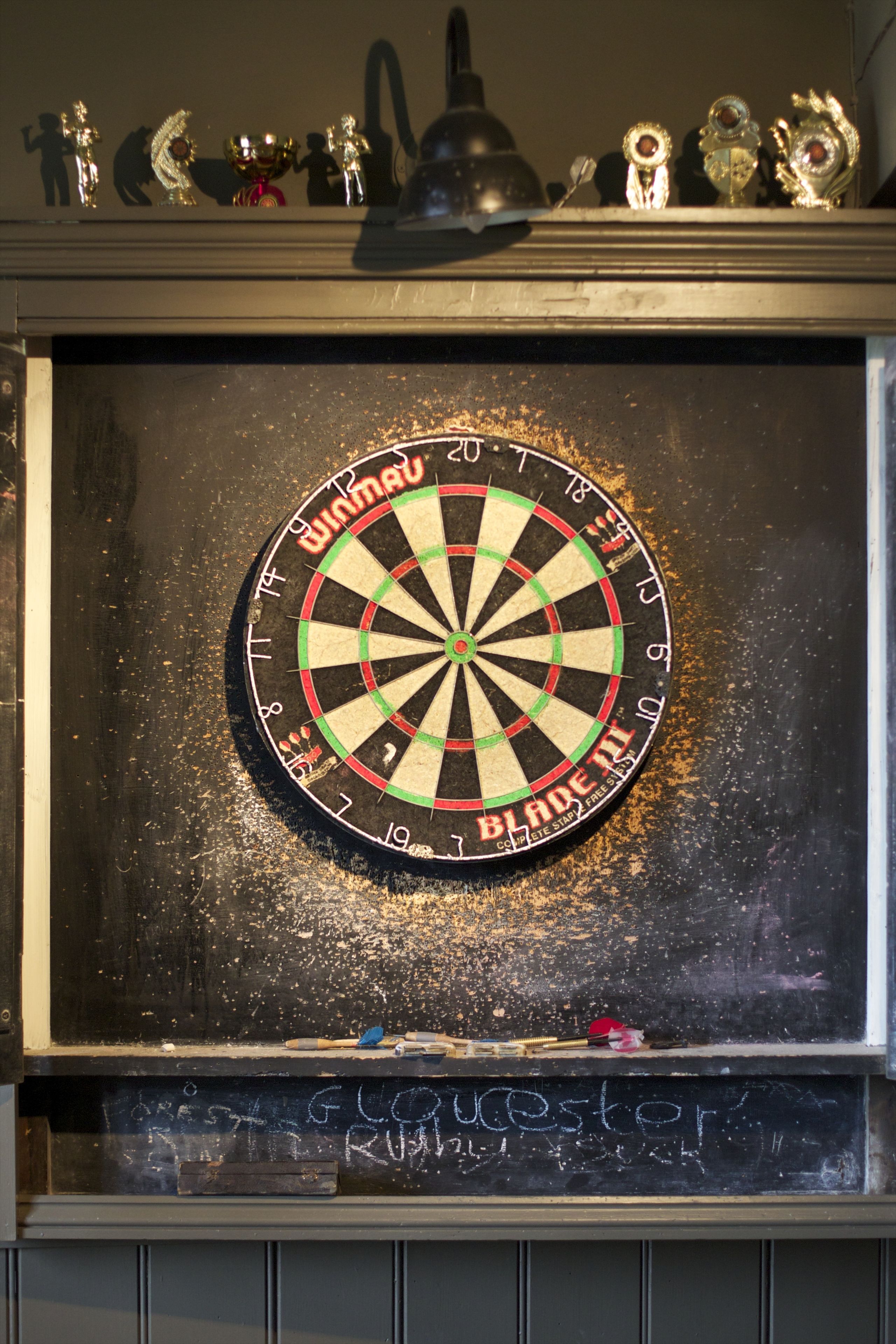 A dartboard mounted on a wall with a chalkboard below it.